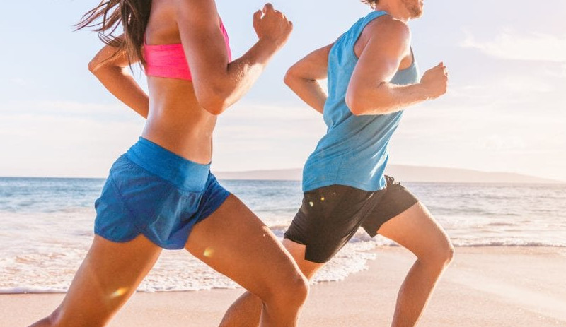 man and a women in pink and blue wearing shorts exercising running on the beach on a nice summer day
